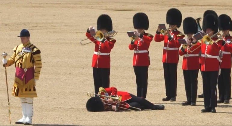 Guarda real tenta tocar trombone no chão após desabar durante desfile